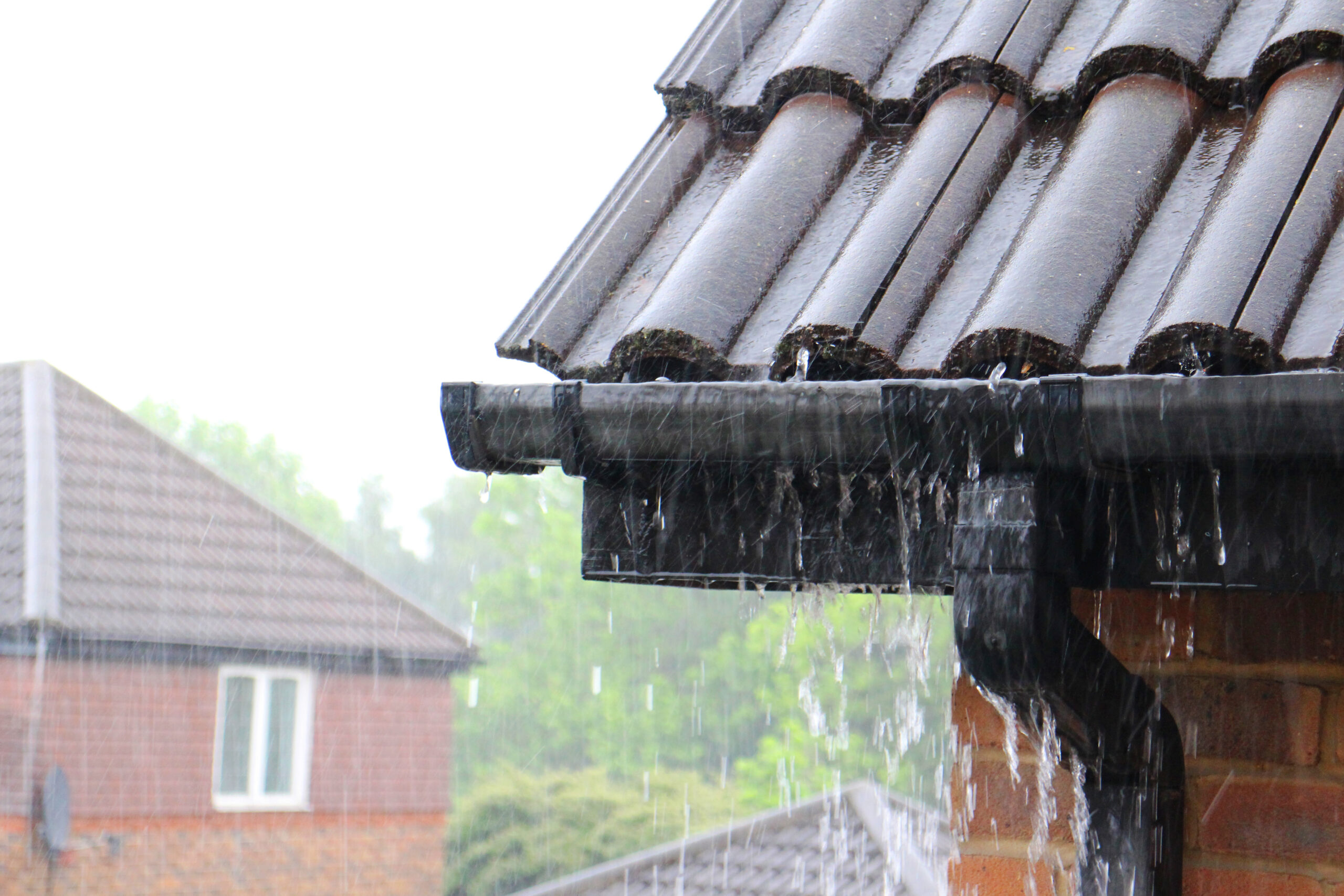 A close-up of a house's gutters during a rainy summer, with guttering in view.