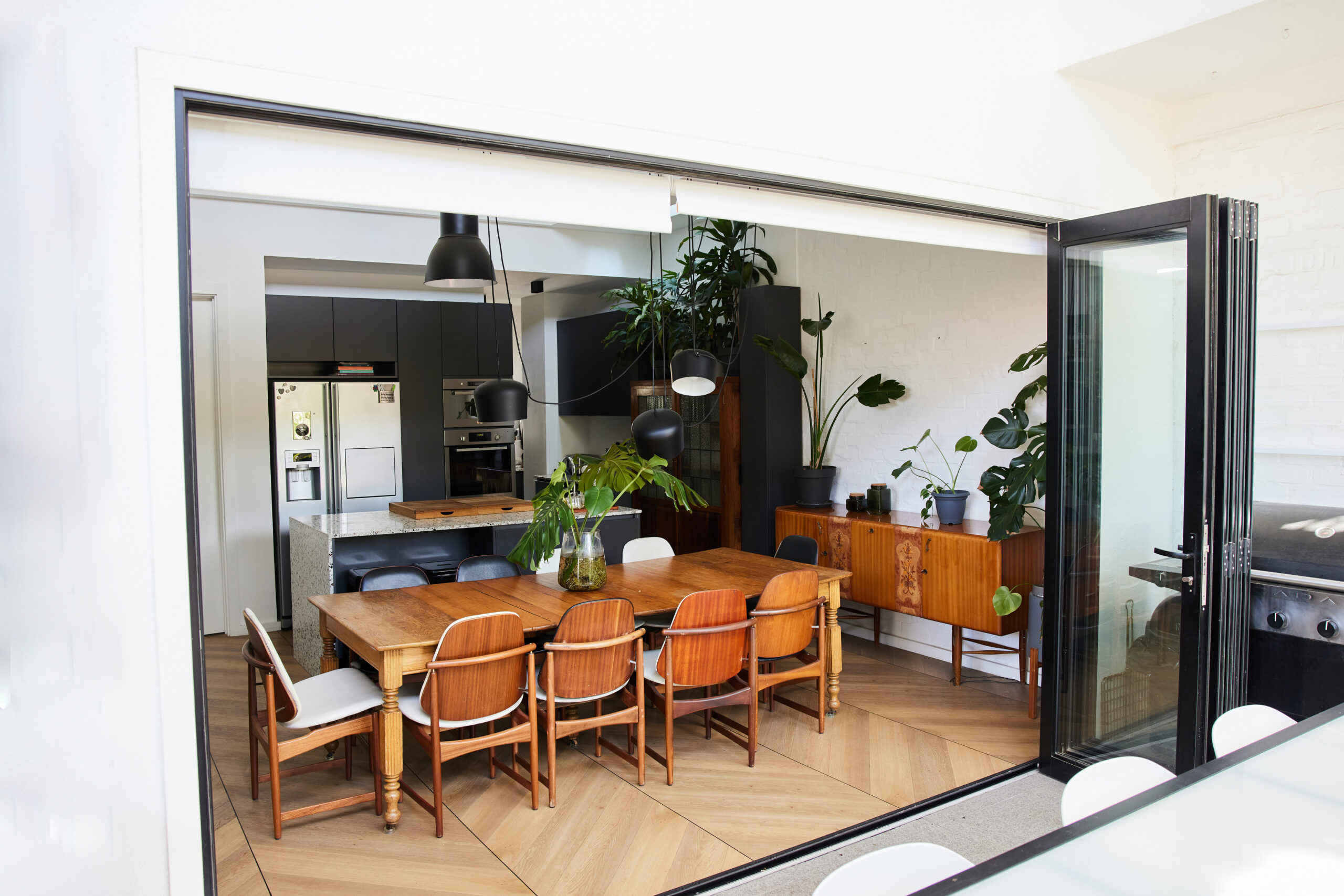 Table and chairs in an open plan dining area of a home next to the open folding doors of a sunny patio